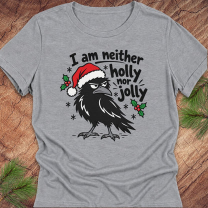 Athletic heather gray women's relaxed t-shirt with a grumpy raven in a Santa hat surrounded by holly and snowflakes and the words I am neither holly nor jolly, laid flat on a rustic wood background with pine branches.