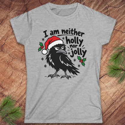 Sport grey women's t-shirt with a grumpy raven in a Santa hat surrounded by holly and snowflakes and the words I am neither holly nor jolly, laid flat on a rustic wood background with pine branches.