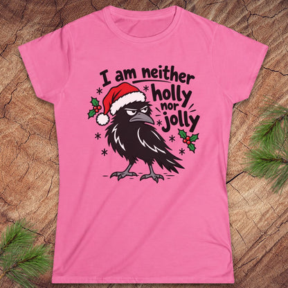 Azalea pink women's t-shirt with a grumpy raven in a Santa hat surrounded by holly and snowflakes and the words I am neither holly nor jolly, laid flat on a rustic wood background with pine branches.