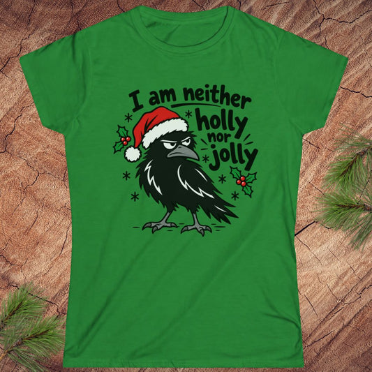Irish green women's t-shirt with a grumpy raven in a Santa hat surrounded by holly and snowflakes and the words I am neither holly nor jolly, laid flat on a rustic wood background with pine branches.