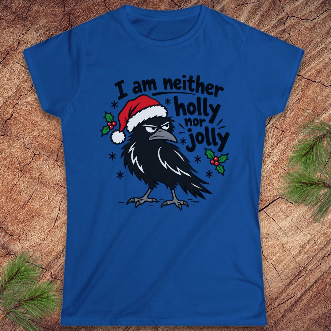Royal blue women's t-shirt with a grumpy raven in a Santa hat surrounded by holly and snowflakes and the words I am neither holly nor jolly, laid flat on a rustic wood background with pine branches.