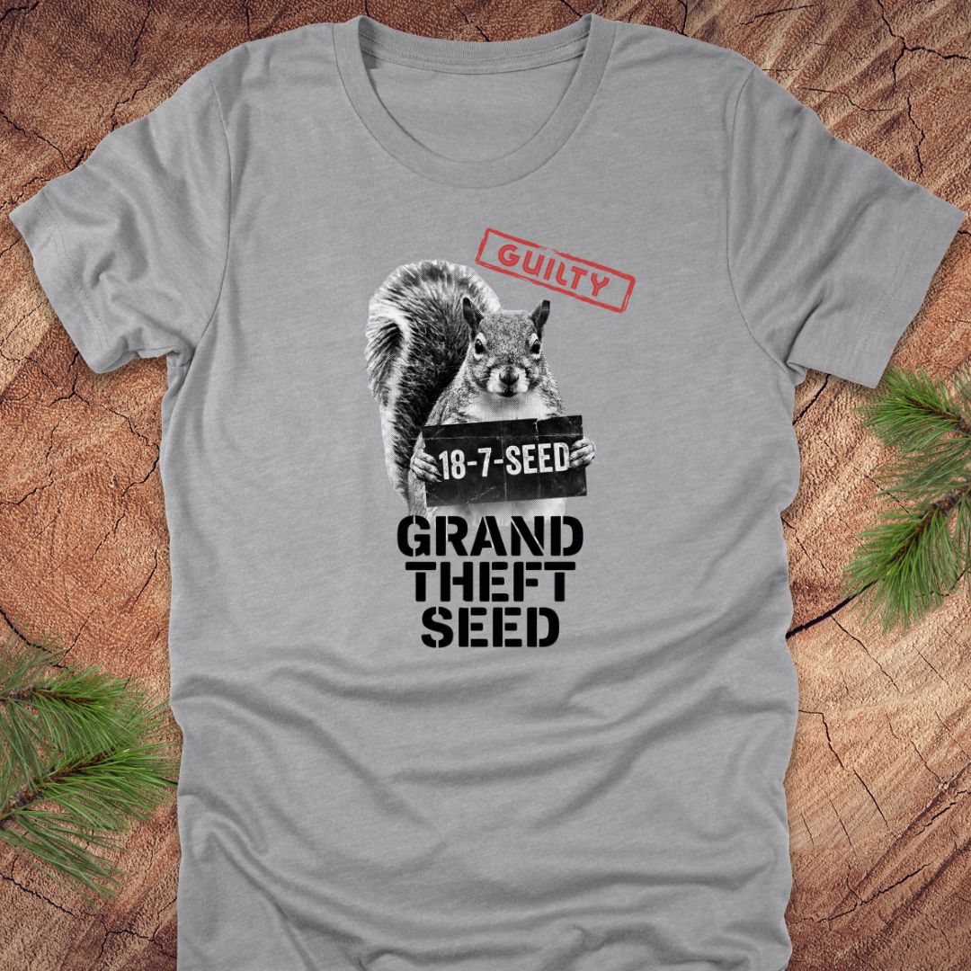Gray t-shirt with a squirrel holding a seed packet graphic and text, 'guilty. grand theft seed'on a wooden surface.