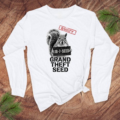 White long-sleeve shirt with a graphic of a squirrel holding a seed packet and text, 'guilty. grand theft seed' on a wooden surface.