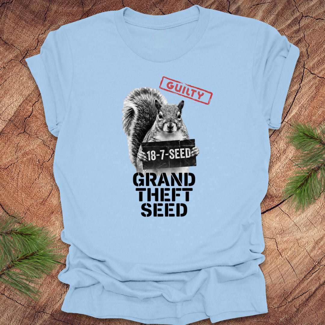 Baby blue t-shirt with a squirrel holding a seed packet graphic and text, 'guilty. grand theft seed'on a wooden surface.