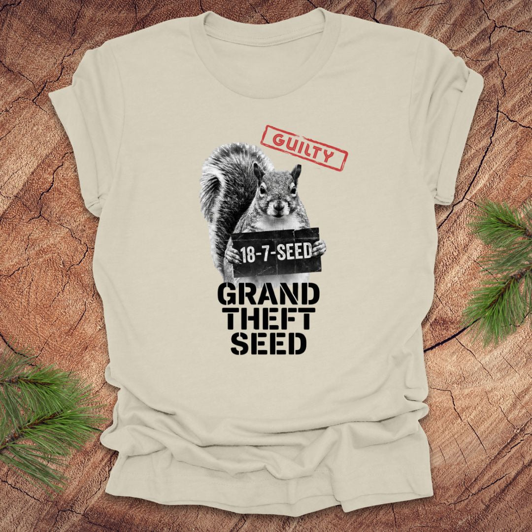 Beige t-shirt with a squirrel holding a seed packet graphic and text, 'guilty. grand theft seed'on a wooden surface.