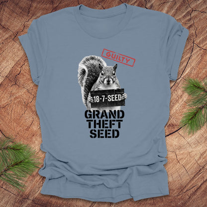 Steel blue t-shirt with a squirrel holding a seed packet graphic and text, 'guilty. grand theft seed'on a wooden surface.
