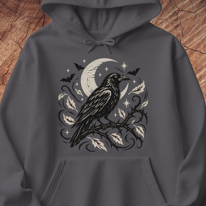 A dark gray hoodie featuring a gothic-style graphic print of a black raven perched on a branch with a crescent moon, bats, and stars, displayed against a textured wood background.