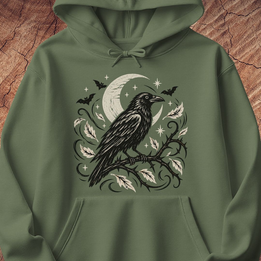 An olive green pullover hoodie featuring a detailed black and white graphic of a raven perched on a branch with leaves, a crescent moon, bats, and stars, displayed against a textured brown wood background.