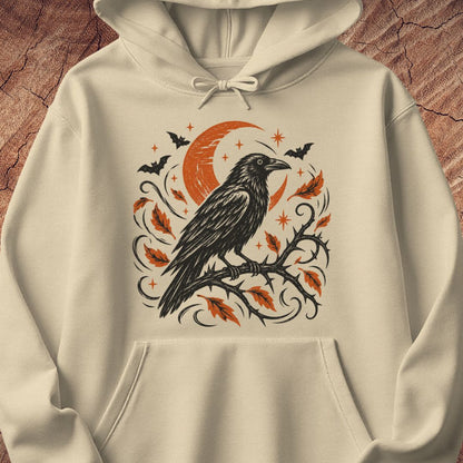 An off-white hooded sweatshirt featuring a detailed graphic print of a black raven perched on a branch with orange leaves, a crescent moon, and bats, displayed against a textured brown wood background.