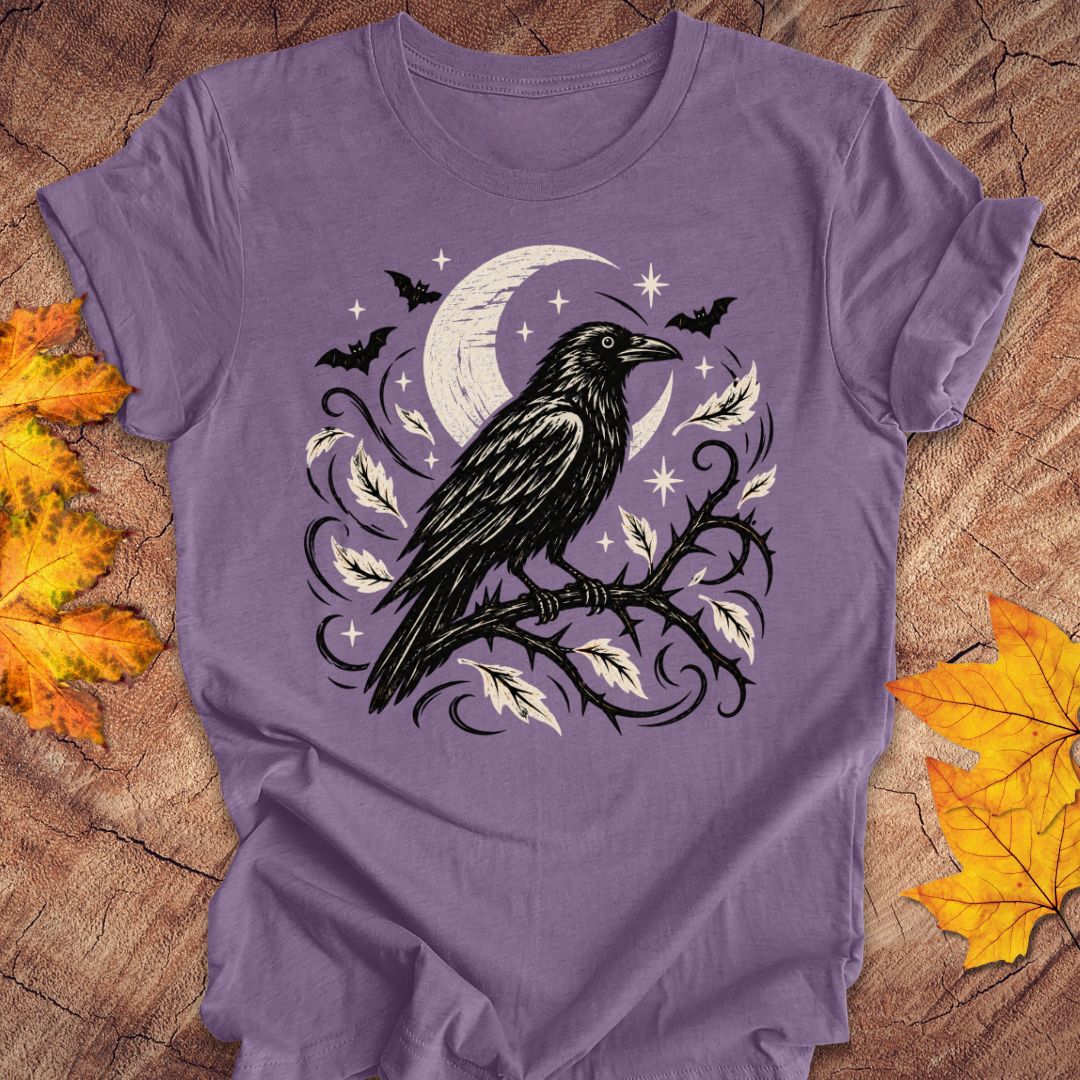 A purple short-sleeve t-shirt with a gothic raven graphic, displayed flat on a rustic wood background with autumn leaves.