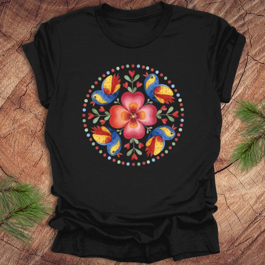 Black t-shirt with a colorful floral and bird design on a wooden surface.