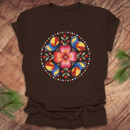 Brown t-shirt with a colorful floral and bird design on a wooden surface.