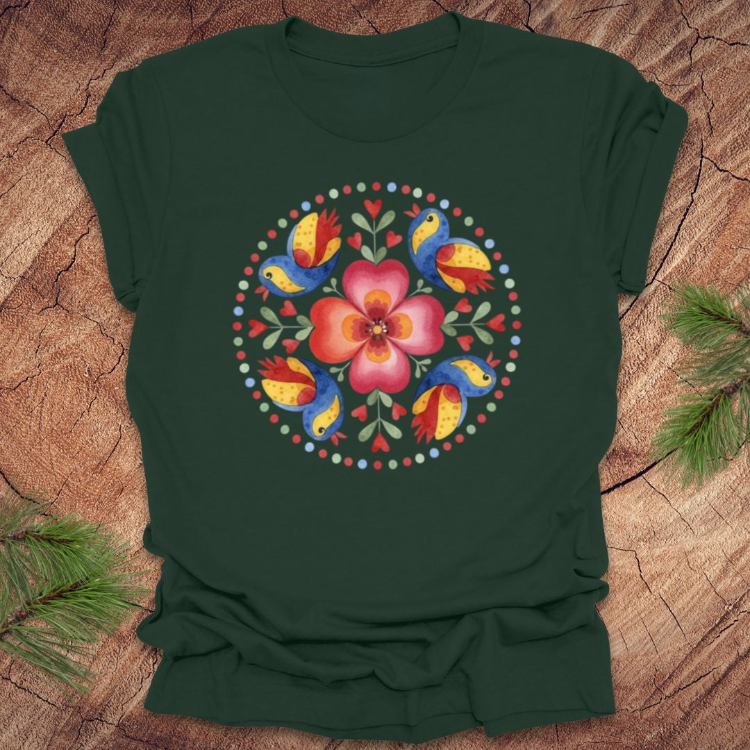 Green t-shirt with a colorful floral and bird design on a wooden surface.