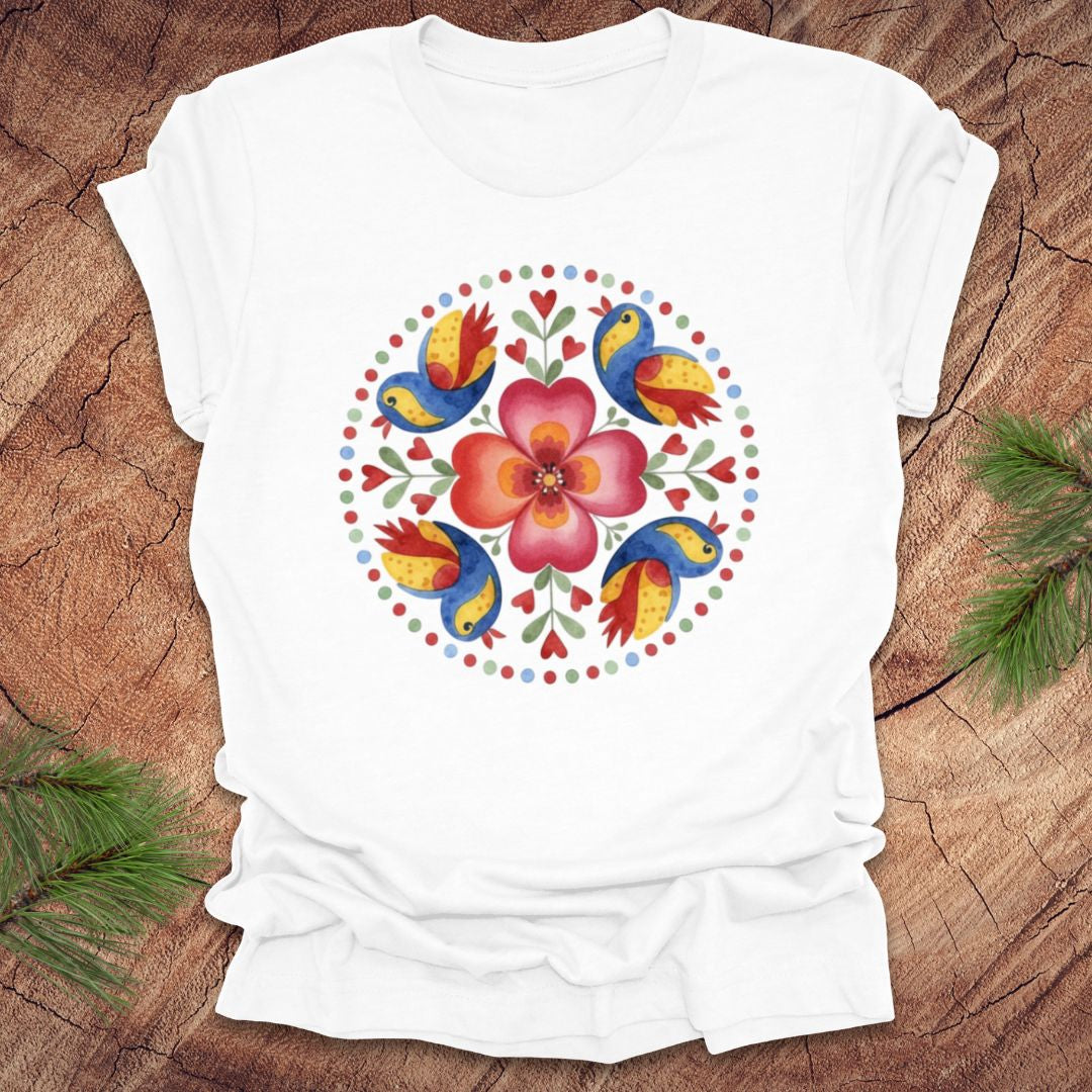 White t-shirt with colorful floral and bird design on a wooden surface