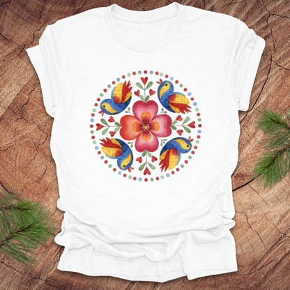 White t-shirt with colorful floral and bird design on a wooden surface
