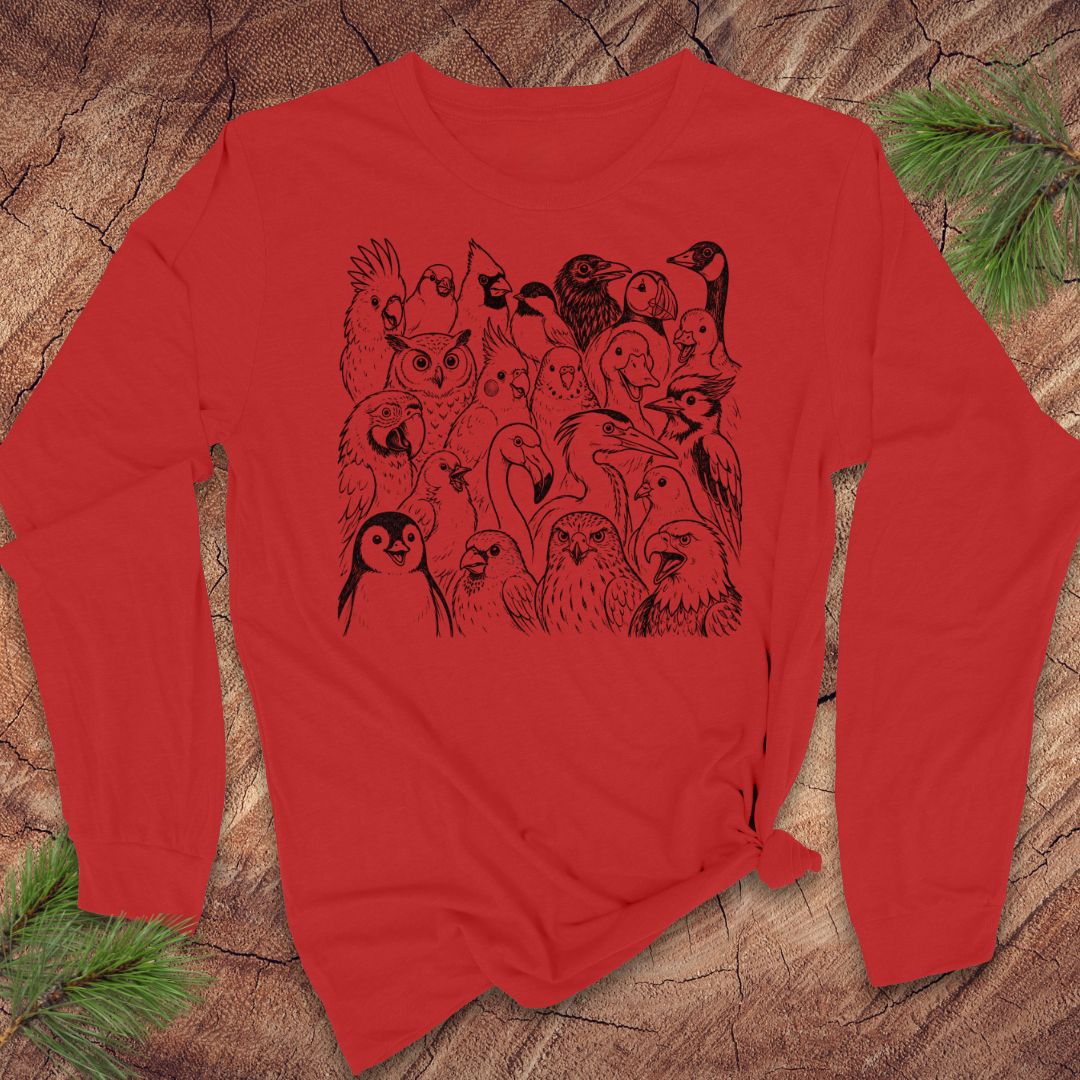 A red long-sleeve t-shirt with a black graphic print of various birds, laid flat on a rustic wood background with pine needles.