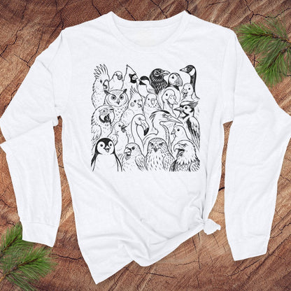 A white long-sleeve t-shirt with a black line art graphic of various birds, displayed flat on a rustic wood background with pine branches.