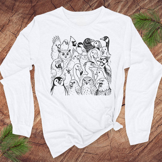 A white long-sleeve t-shirt with a black line art graphic of various birds, displayed flat on a rustic wood background with pine branches.