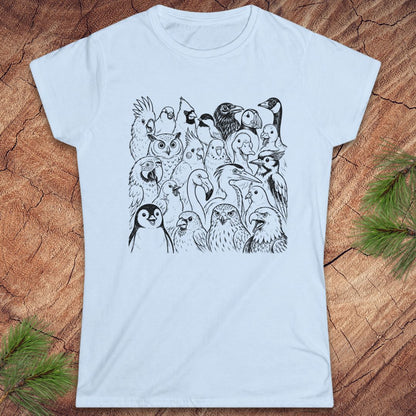 A light blue short-sleeve crewneck t-shirt featuring a black line art graphic of a dense group of various birds, laid flat on a textured wood background with pine needles in the corners.