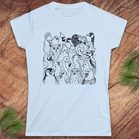A light blue short-sleeve crewneck t-shirt featuring a black line art graphic of a dense group of various birds, laid flat on a textured wood background with pine needles in the corners.