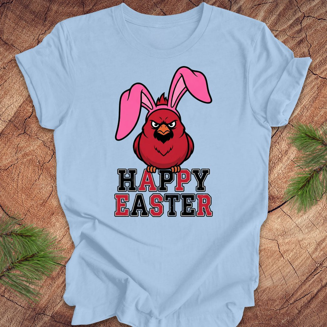 Light blue t-shirt with a cardinal wearing bunny ears and 'Happy Easter' text on a wooden surface.