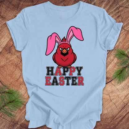 Light blue t-shirt with a cardinal wearing bunny ears and 'Happy Easter' text on a wooden surface.