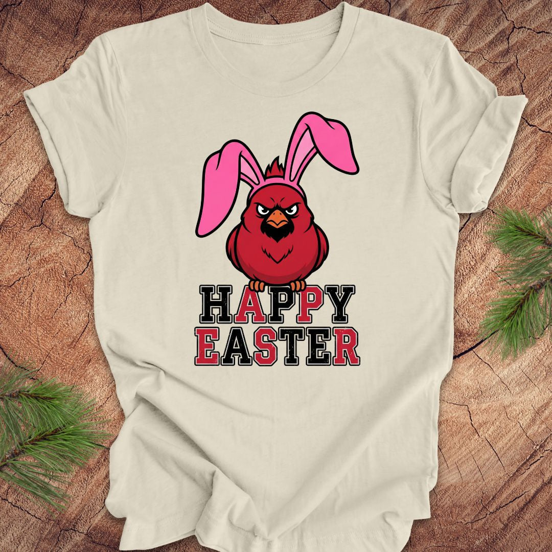 Beige t-shirt with a cardinal wearing bunny ears and 'Happy Easter' text on a wooden surface.
