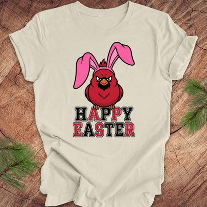 Beige t-shirt with a cardinal wearing bunny ears and 'Happy Easter' text on a wooden surface.