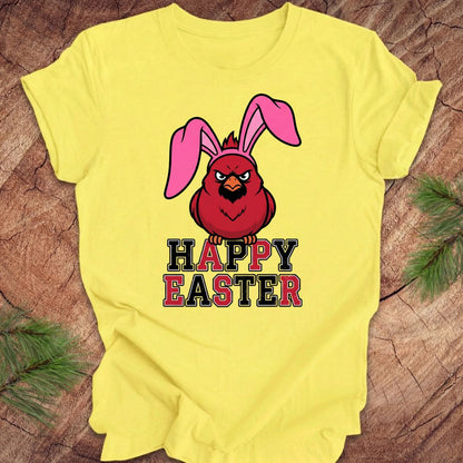 Yellow t-shirt with a cardinal wearing bunny ears and 'Happy Easter' text on a wooden surface.