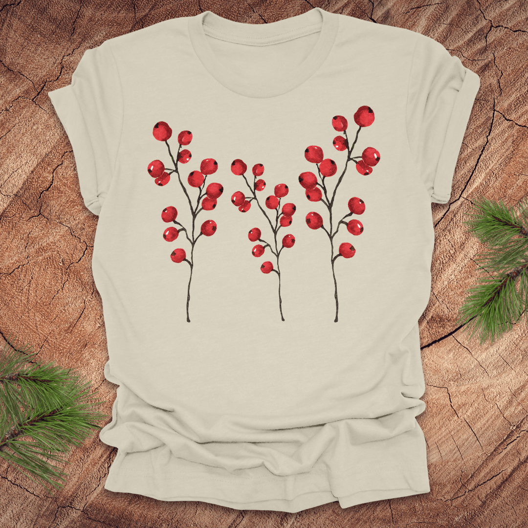 Beige t-shirt with three tall holly berry branches on a wood background with pine branches.