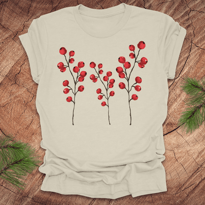 Beige t-shirt with three tall holly berry branches on a wood background with pine branches.