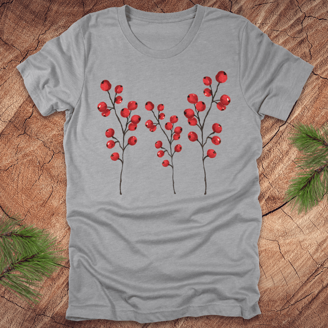 Grey t-shirt with three tall holly berry branches on a wood background with pine branches.