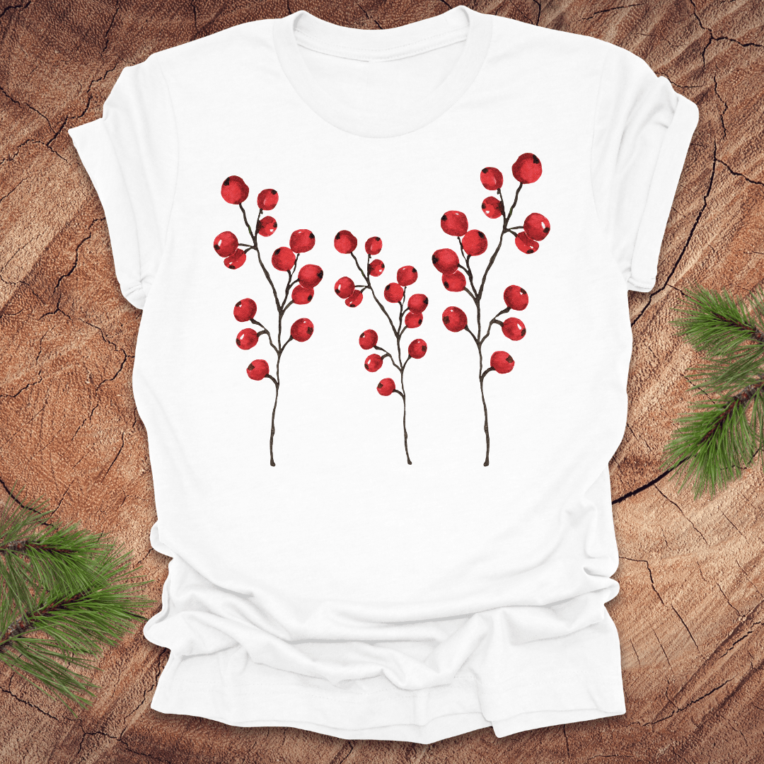 White t-shirt with three tall holly berry branches on a wood background with pine branches.