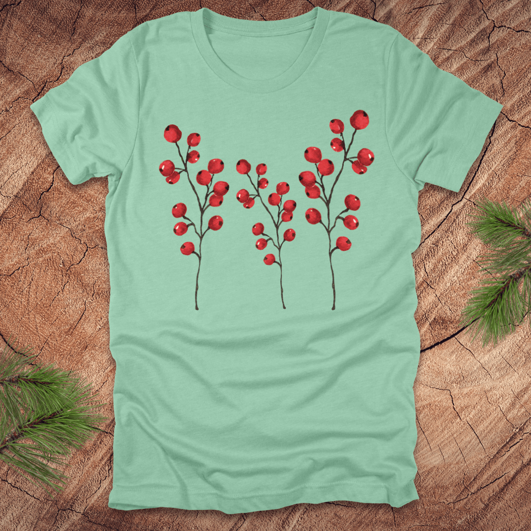Mint green t-shirt with three tall holly berry branches on a wood background with pine branches.