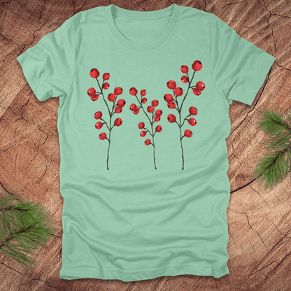 Mint green t-shirt with three tall holly berry branches on a wood background with pine branches.