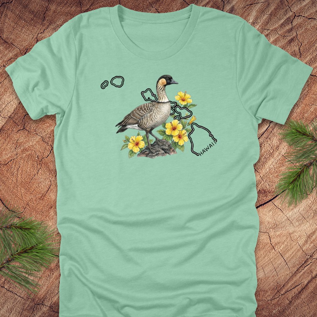 Mint green t-shirt with a nene goose and hibiscus design over the outline of the state of Hawaii on a wooden surface