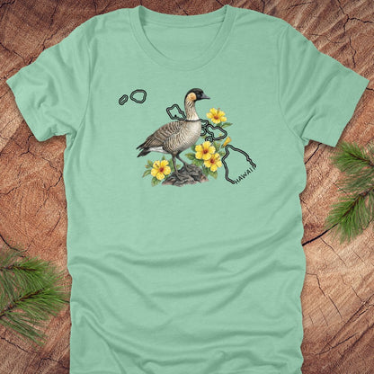 Mint green t-shirt with a nene goose and hibiscus design over the outline of the state of Hawaii on a wooden surface