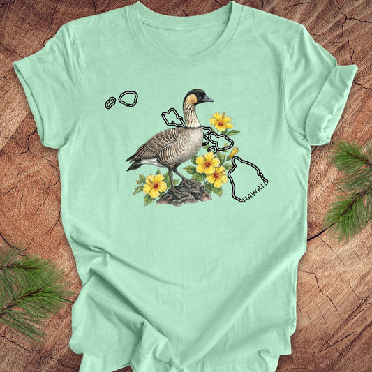 Mint green t-shirt with a nene goose and hibiscus design over the outline of the state of Hawaii on a wooden surface