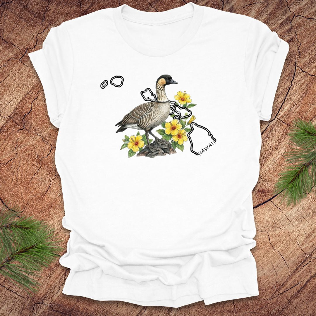 White t-shirt with a nene goose and hibiscus design over the outline of the state of Hawaii on a wooden surface
