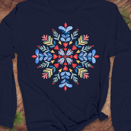 A navy blue long-sleeve t-shirt with a colorful, symmetrical floral snowflake graphic printed on the chest, laid flat on a rustic wood background.