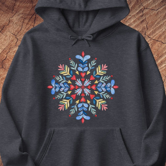 A dark heather gray hoodie featuring a colorful, symmetrical snowflake graphic on the chest, displayed flat against a rustic wood background.