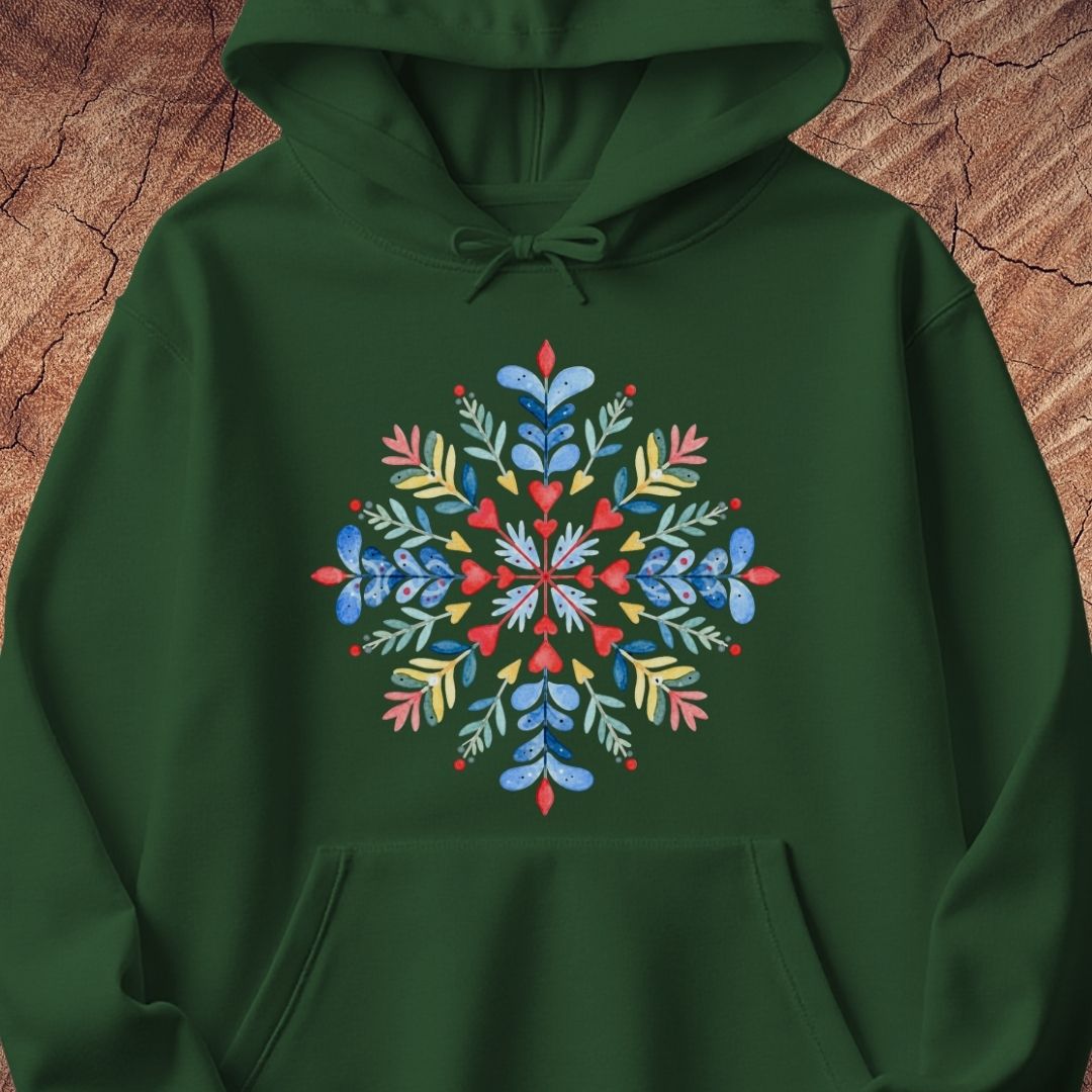 A dark green pullover hoodie featuring a colorful, symmetrical floral snowflake graphic printed on the chest, displayed against a textured brown wood background.