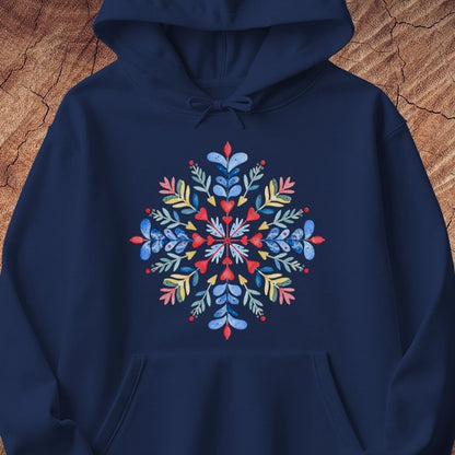 A navy blue pullover hoodie featuring a colorful, symmetrical snowflake design printed on the chest, displayed against a rustic wood background.