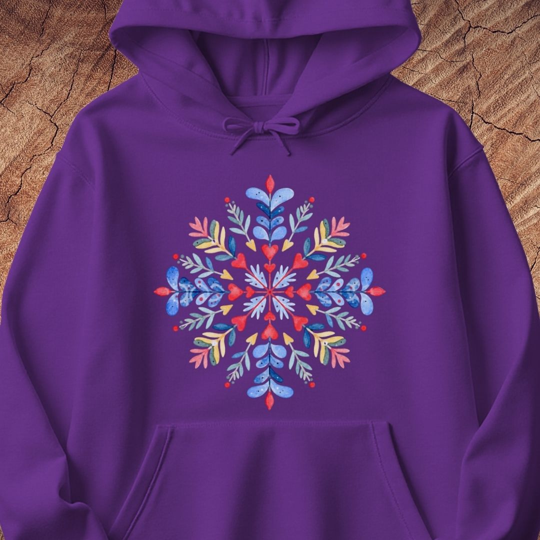 A purple pullover hoodie with a colorful, symmetrical floral snowflake graphic printed on the chest, displayed flat against a rustic wood background.