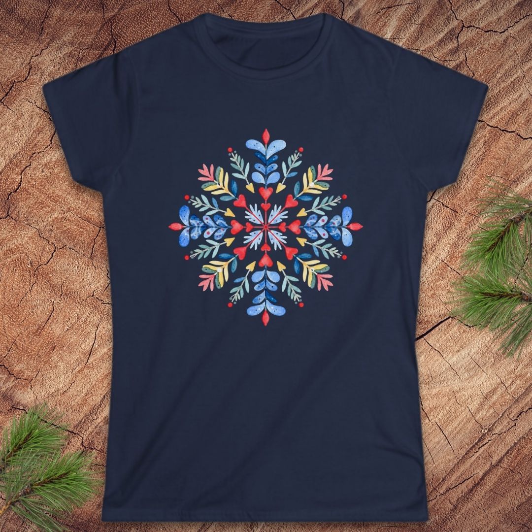 A navy blue short-sleeve crewneck t-shirt featuring a colorful, symmetrical bohemian-style floral mandala print on the chest. The shirt is displayed flat on a textured brown wood background with pine needles in the corners.