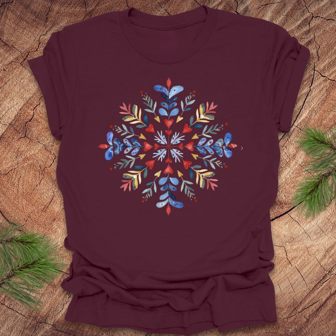 Maroon t-shirt with a colorful snowflake and floral design on a wooden surface