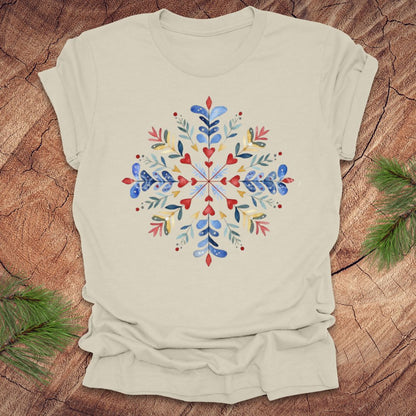 Beige t-shirt with a colorful snowflake and floral design on a wooden surface