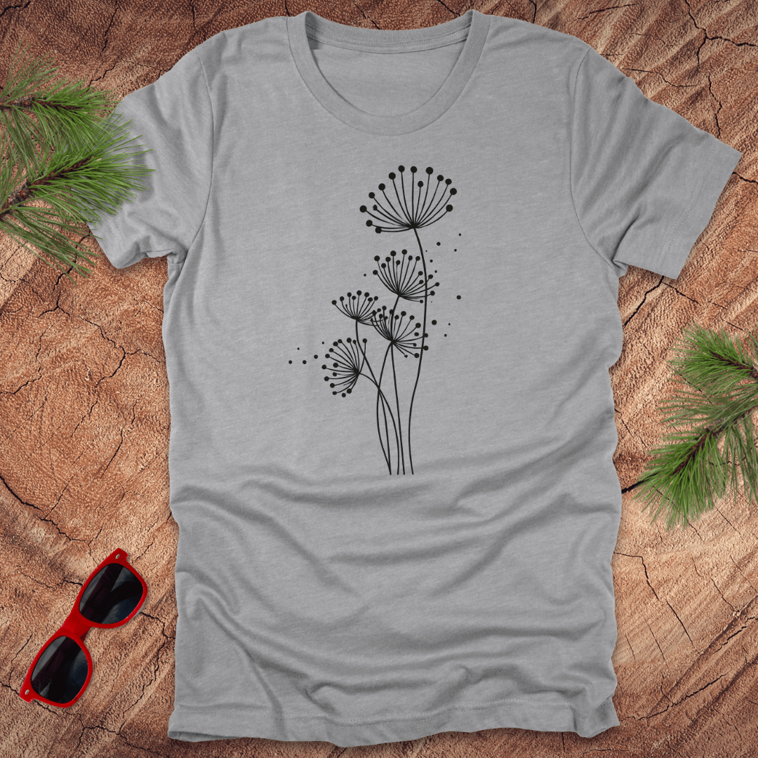 Gray t-shirt with black floral dandelion design on a wooden surface with sunglasses and greenery.