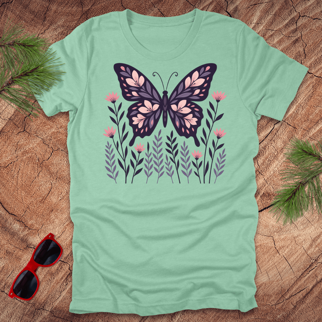 mint green t-shirt with a butterfly and flower design on a wooden surface with sunglasses and leaves.