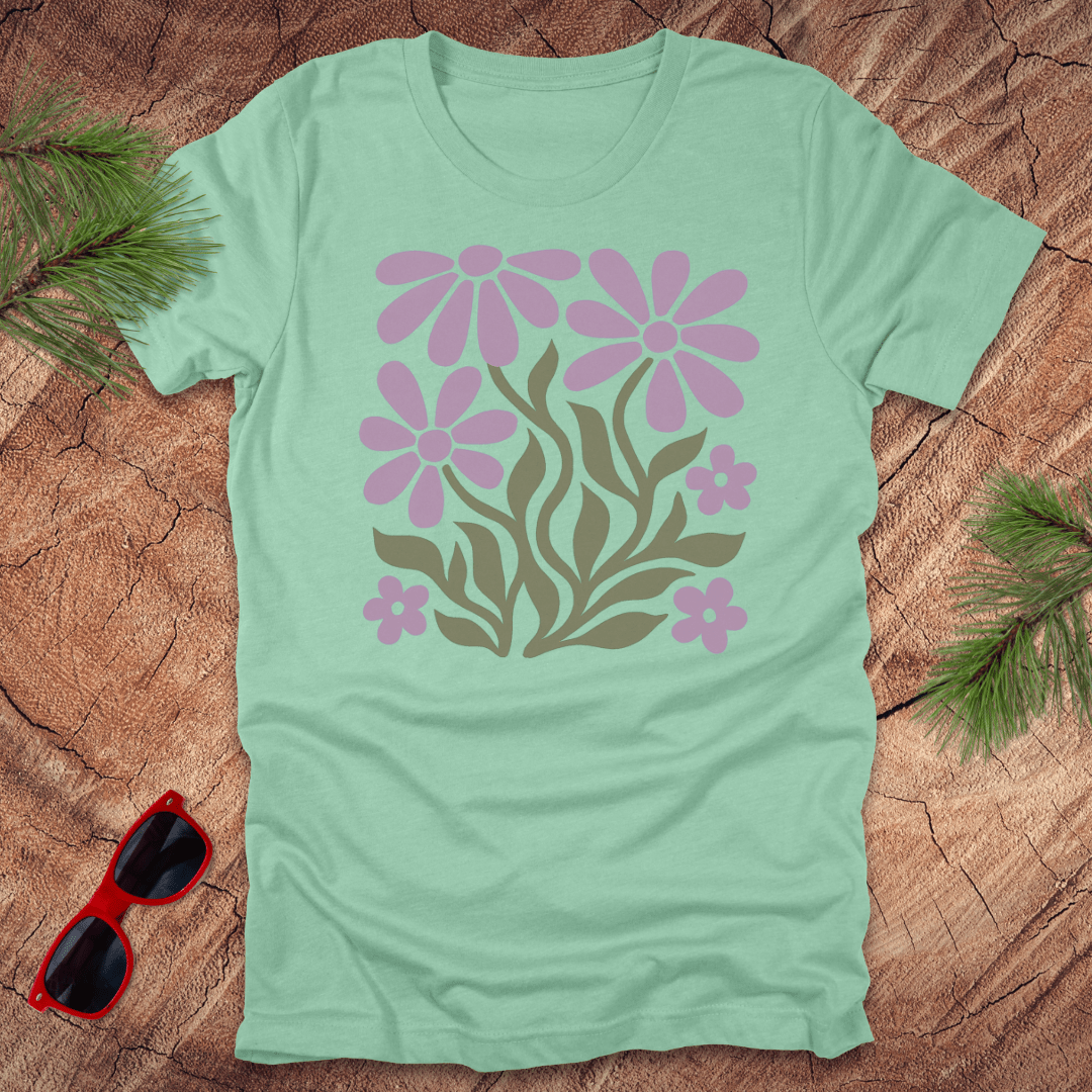 Light green t-shirt with pink floral design on a wooden surface with sunglasses and greenery.